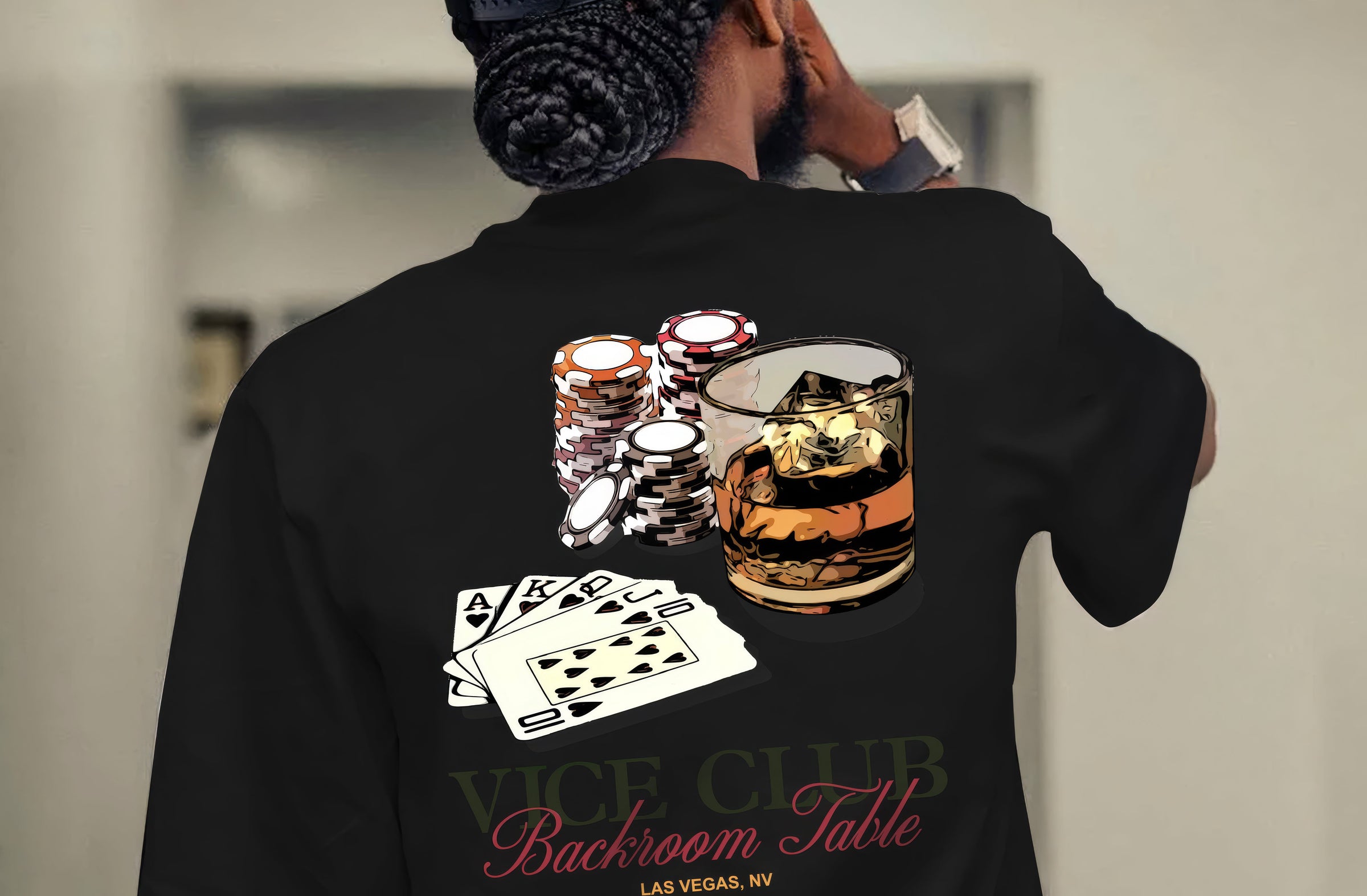 Rear view of man wearing black Vice Club t-shirt with casino-inspired graphic featuring playing cards, poker chips and whiskey glass in a moody lifestyle setting.