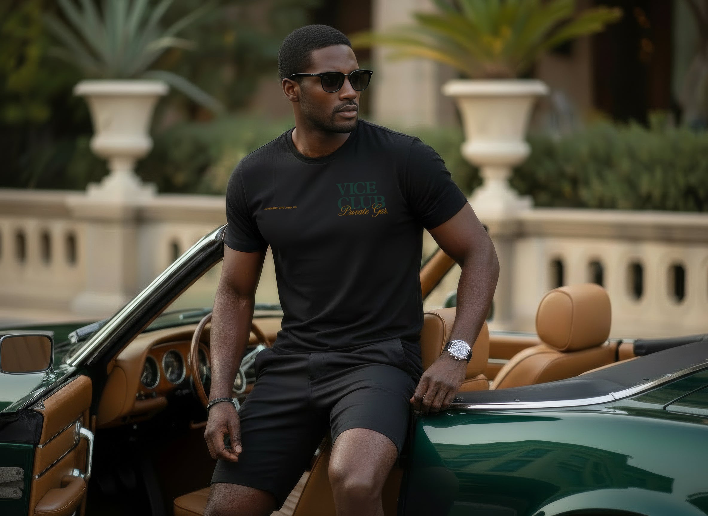 Rear view of man wearing black Vice Club t-shirt featuring leopard and vintage car graphic, set in a dark cinematic luxury garage environment.